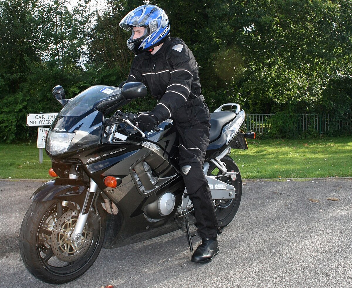 Motorista con casco integral, chaqueta y guantes sobre una moto